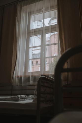 a bedroom with a window with white curtains and a bed at Pokoje Gościnne Domu Pielgrzyma w Supraślu in Supraśl