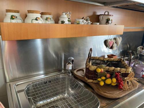 a kitchen sink with a basket of fruit on a shelf at Jolie maison in Montalbano Jonico
