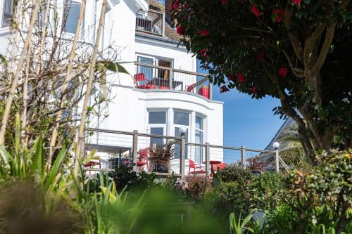 a white building with red chairs and a balcony at Chelsea House Holiday Apartments in Falmouth