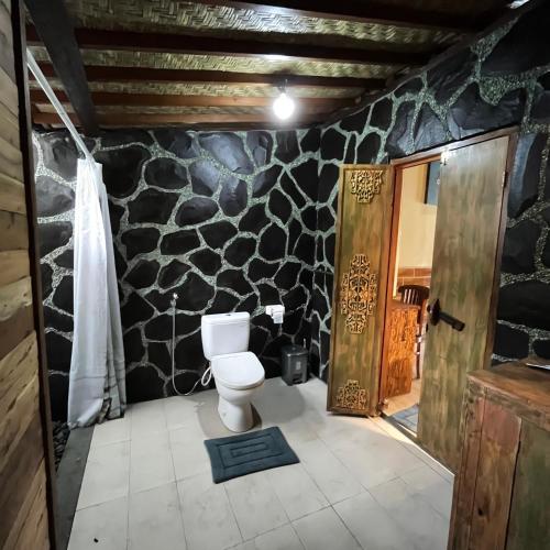 a bathroom with a toilet and a stone wall at Yoga Maya Villa in Gianyar