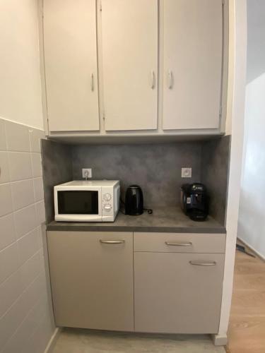 une cuisine avec des placards blancs et un four micro-ondes sur un comptoir dans l'établissement Centre historique à 2 pas du musée RIGAUD, à Perpignan