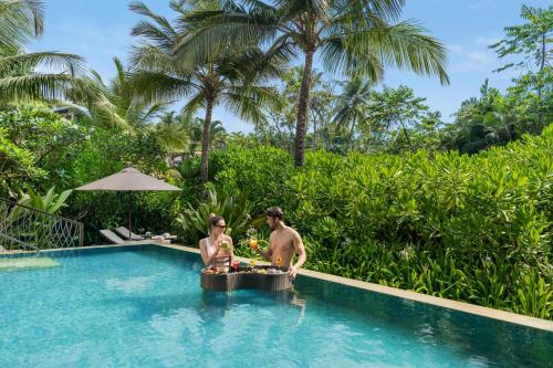 Un hombre y una mujer sentados en una piscina en The St. Regis Goa Resort, en Cavelossim