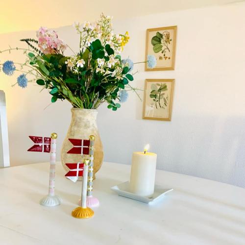 a vase with flowers and a candle on a table at Idyllisk sommerhus tæt ved Blåvand in Billum