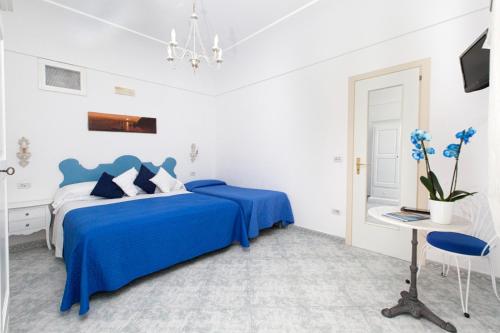 a white bedroom with a blue bed and a desk at La Maliosa Positano in Positano