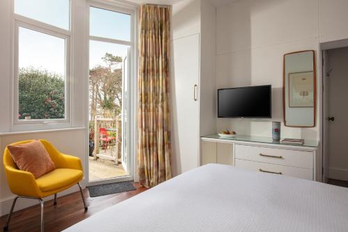 a bedroom with a bed and a yellow chair and a window at Chelsea House Holiday Apartments in Falmouth