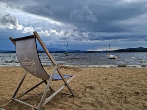 a chair sitting on a beach with a boat in the water at Relax Vila Lipno- Studio u pláže Windy Point in Černá v Pošumaví