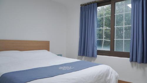 a bedroom with a bed with blue curtains and a window at Sweet Stay Pension in Seogwipo