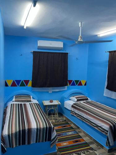 two beds in a room with blue walls and a table at AnDy Nubian Guest House in Aswan