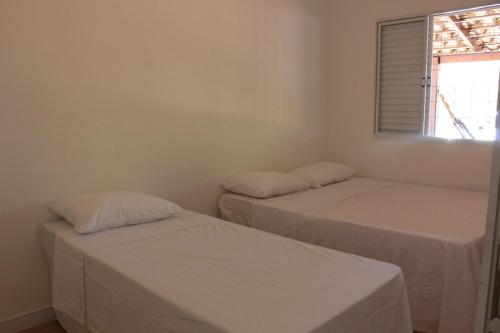 two beds in a white room with a window at Casa na fazenda inteira ou quartos individuais no Hostel Recanto da Felicidade Paraopeba in Paraopeba