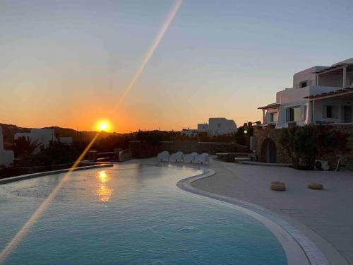 a pool with chairs and the sunset in the background at The Mykonian Escape in Mýkonos City