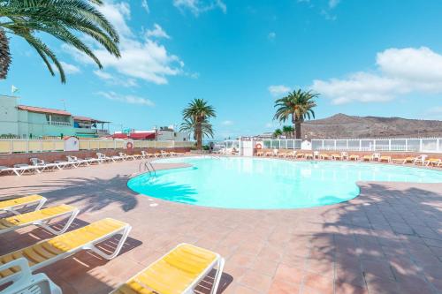 a swimming pool with lounge chairs and palm trees at Private Jacuzzi & vista al mar in Mogán