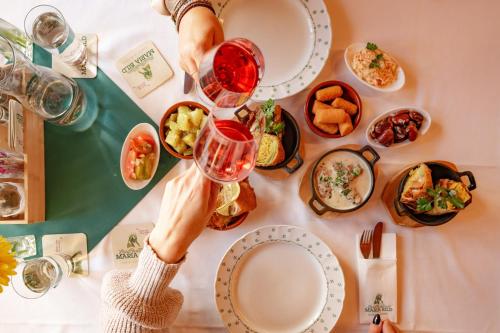 a table with plates of food and a person holding a wine glass at Landrasthaus Maria Bild in Maria Bild
