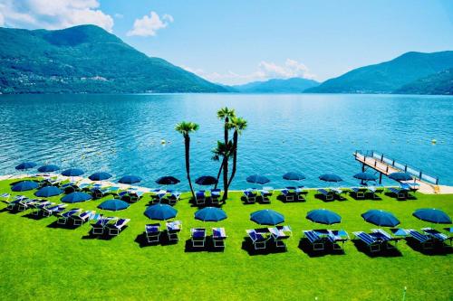 a group of lawn chairs and umbrellas next to a lake at Spectacular penthouse with lake views in central Brissago in Brissago