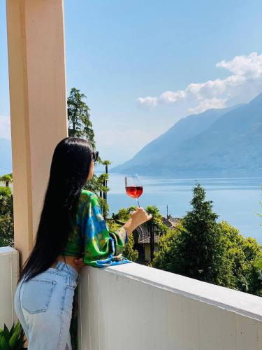a woman sitting on a ledge holding a glass of wine at Sunny modern Apartment Lake View Relax in Brissago