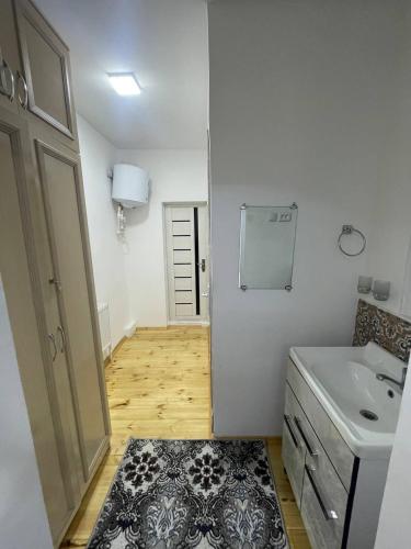 a white bathroom with a sink and a door with a rug at Olimxon Guest House in Bukhara