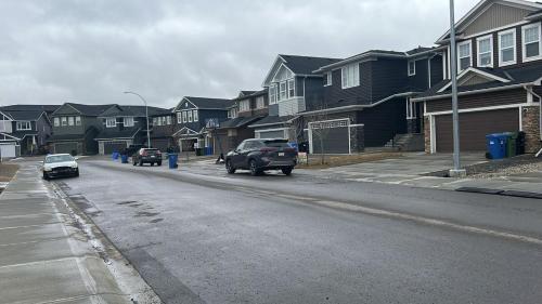 a street with cars driving down a street with houses at Haven Lodge, 2BR Brand New Basement Suite in Calgary