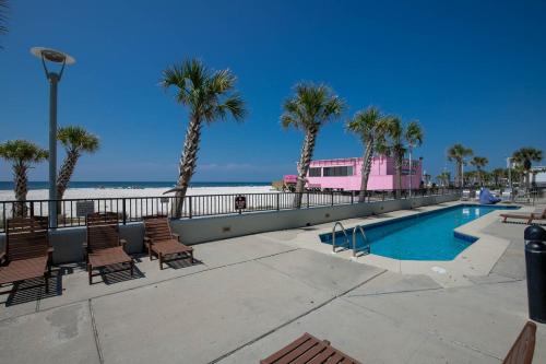 a pool with chairs and palm trees next to the beach at Phoenix All Suites Hotel in Gulf Shores
