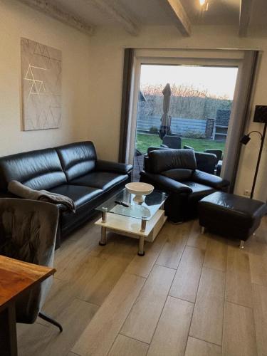 a living room with black leather couches and a table at Wood&Stone - Modernes Haus in Seenähe am Tankumsee mit Terrasse, Outdoorküche, Kamin, Homeoffice Bereich & voll ausgestatteter Küche im Naherholungsgebiet in Isenbüttel