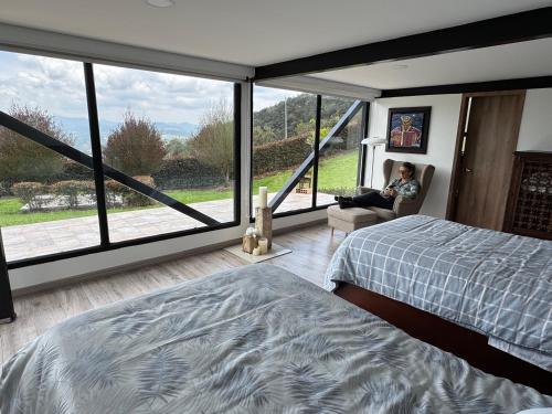 Ein Mann sitzt in einem Stuhl in einem Schlafzimmer mit einem großen Fenster in der Unterkunft El Tabano Eco Hotel in La Calera