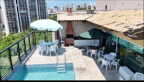 a balcony with a swimming pool with chairs and an umbrella at Cobertura Luxuosa, pe na areia - Exclusividade na Praia do Tombo, Guarujá, a Mais Premiada com Bandeira Azul no Brasil in Guarujá
