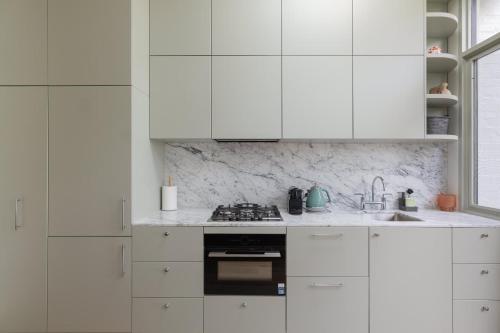 a white kitchen with white cabinets and a stove at Exquisite Modern 3 Bed Home in Newtown w Parking in Sydney