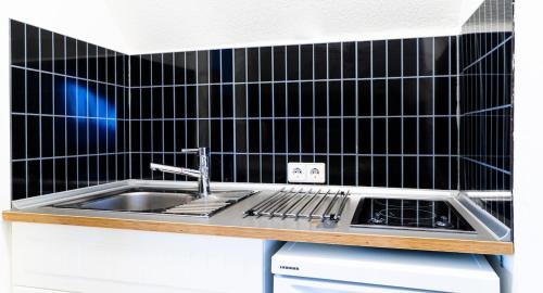 シュタイネンブロンにあるStayIN Apartment near Stuttgartの黒いタイル張りの壁、シンク付きのキッチンが備わります。