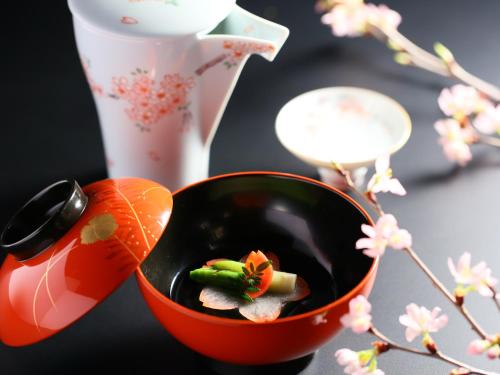 a red bowl with vegetables in it next to a vase at Hotel Tamanoyu in Matsumoto