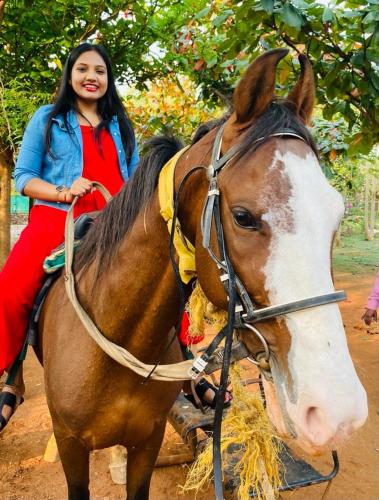 a young girl sitting on a horse eating hay at 1000 SILVERS -Farm Stay in Mysore