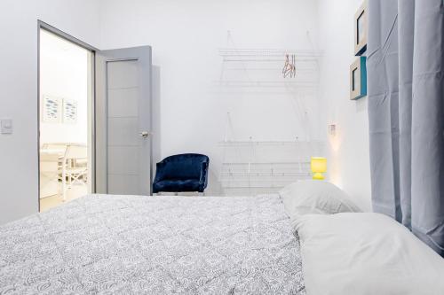 a white bedroom with a bed and a blue chair at El patio de Lucia, center 4 people Las Terrenas in Las Terrenas