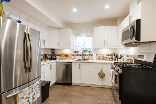 a kitchen with white cabinets and a stainless steel refrigerator at Beautiful Vancouver Cedar Cottage House in Vancouver