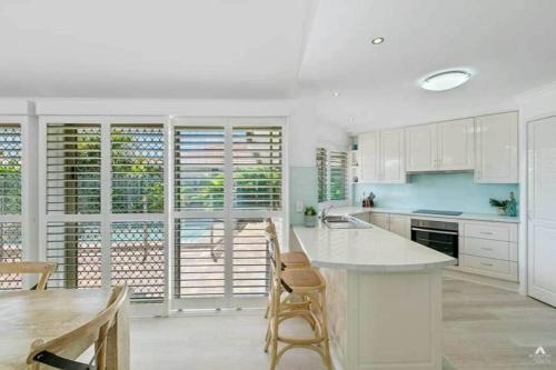a kitchen with white cabinets and a table and chairs at Bokarina Pool House - Relaxed Coastal Living in Bokarina