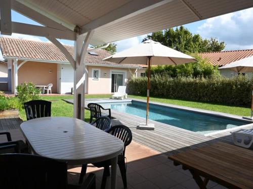 une terrasse avec une table, un parasol et une piscine dans l'établissement Maison 4 chambres avec piscine, à 8 min du lac de Sanguinet - FR-1-521-249, à Sanguinet