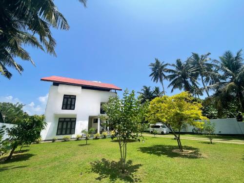 a white house with trees in the yard at Curly Hostel Negombo in Negombo