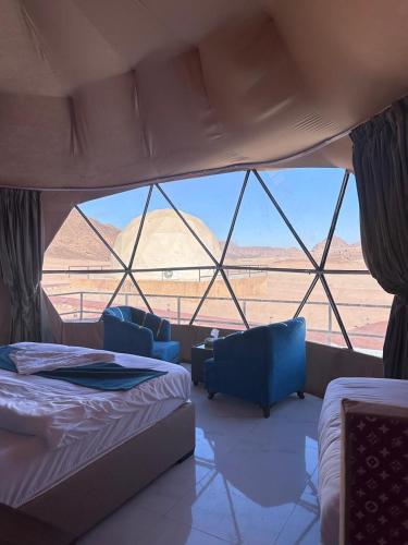a room with a bed and chairs and a view of the desert at Wadi Rum Salman camp in Wadi Rum