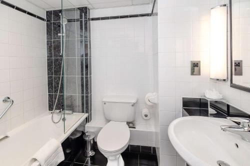 a white bathroom with a toilet and a sink at Hilton London Olympia in London