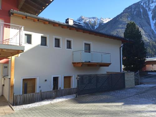 a white building with a fence and mountains in the background at High-quality holiday apartment in Oberkrimml near waterfalls in Krimml