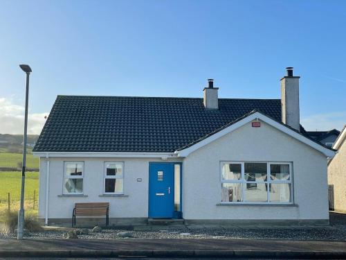 a white house with a blue door and a bench at Portballintrae 3 bedroom cosy coastal bungalow in Portballintrae