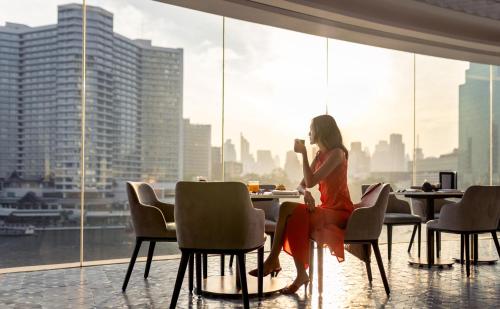 Una mujer con un vestido rojo sentada en una mesa con una bebida. en Millennium Hilton Bangkok, en Bangkok