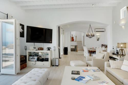 a living room with white furniture and a tv at Blueros - Black Stone Suite in Megas Yialos-Nites