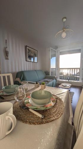 - un salon doté d'une table avec des assiettes et des verres à vin dans l'établissement Le Panoramique, F2- vue imprenable, wifi & parking, à Blonville-sur-Mer