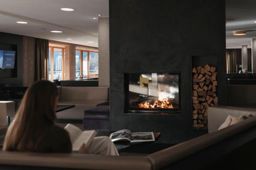 a woman reading a book in front of a fireplace at Das Kronthaler - Adults only in Achenkirch