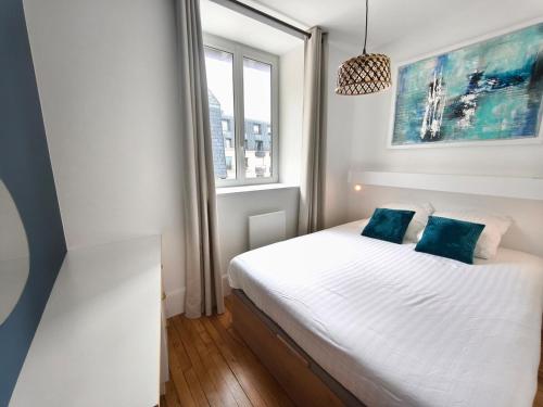 a bedroom with a bed with white sheets and blue pillows at L'Harmonie des Vagues in Granville