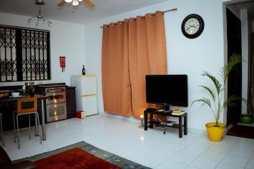 a living room with a tv on a wall with a clock at Royal London Ville Apartment in Tema Community 6 in Tema