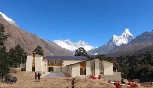 a group of people standing outside a building with mountains in the background at The Himalayan Tyangboche in Lukla