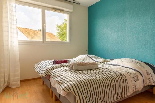 Cet appartement comprend une chambre dotée d'un lit avec un mur bleu et une fenêtre. dans l'établissement FRANCIS LE CARVAL - REZE - balcon - parking, à Rezé