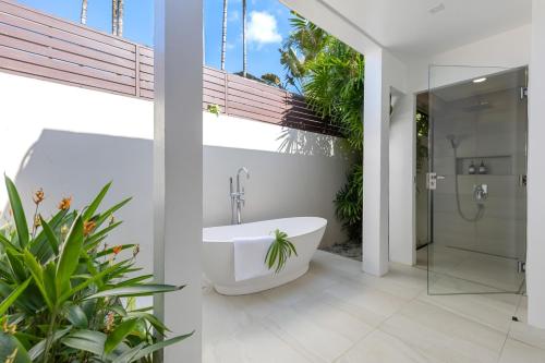 a bathroom with a bath tub and a shower with plants at Bacaya Beachfront Villa in Bang Rak Beach