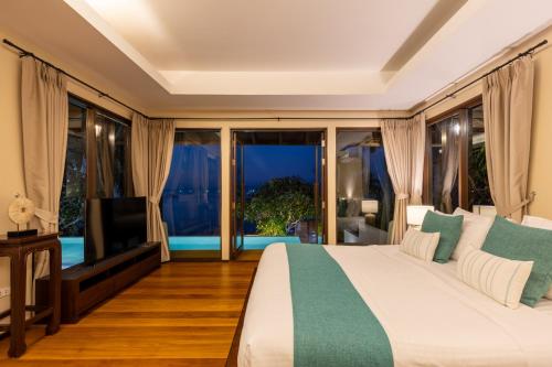 a bedroom with a bed and a tv and windows at Bacaya Beachfront Villa in Bang Rak Beach
