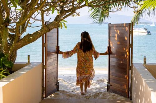 a woman walking through a door on the beach at Bacaya Beachfront Villa in Bang Rak Beach