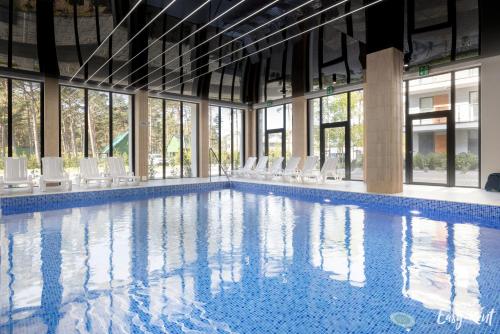a large swimming pool with white chairs and windows at Prestige Red z basenem in Pobierowo