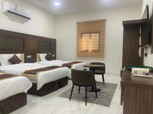 une chambre d'hôtel avec trois lits, un bureau et une télévision dans l'établissement Wind alula, à Al-Ula